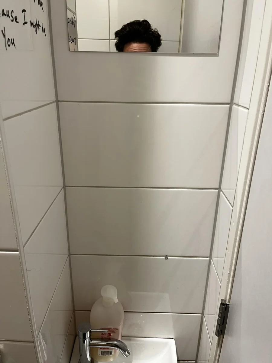 Nízke zrkadlo v kúpeľni odráža vrchnú časť hlavy; viditeľné je umývadlo a mydlo v jasne osvetlenej miestnosti.
