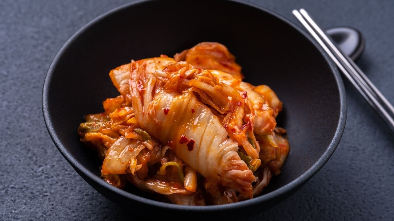 Tradičné kórejské kimchi v čiernej miske na tmavom stole, vedľa sú kovové paličky.