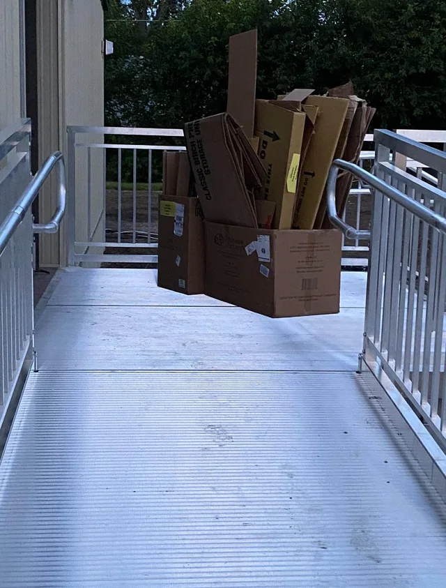 Kartónové krabice uložené na kovovej rampe vedľa budovy, pripravené na recykláciu alebo odvoz.