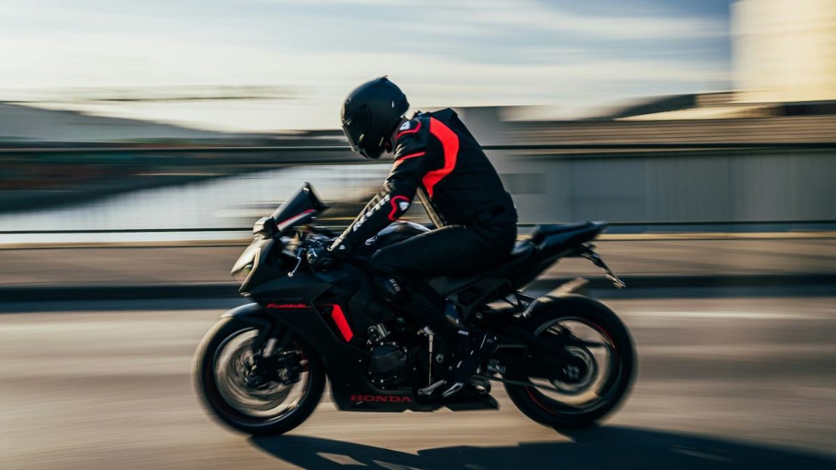 Motorkár na športovej motorke v pohybe na moste, čierno-červené oblečenie, rýchlosť a voľnosť na otvorenej ceste.
