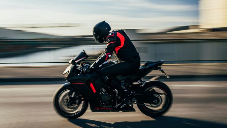 Motorkár na športovej motorke v pohybe na moste, čierno-červené oblečenie, rýchlosť a voľnosť na otvorenej ceste.