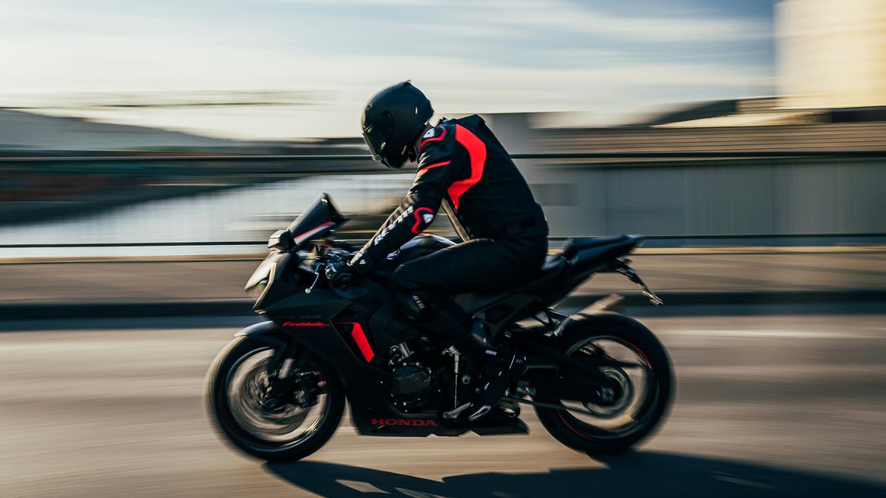 Motorkár na športovej motorke v pohybe na moste, čierno-červené oblečenie, rýchlosť a voľnosť na otvorenej ceste.