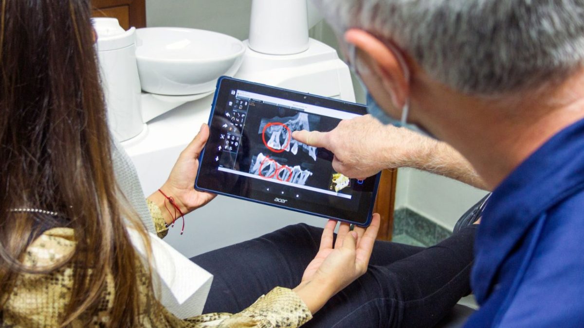 Dentista ukazuje pacientke rentgenový snímok na tablete v stomatologickej ordinácii.