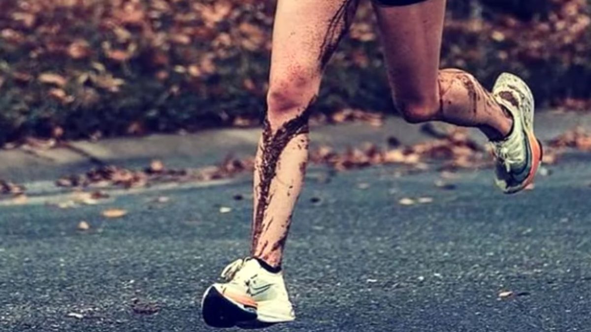 Bežec s blatom na nohách beží po cestnom povrchu, zasadený do jesenného prostredia.
