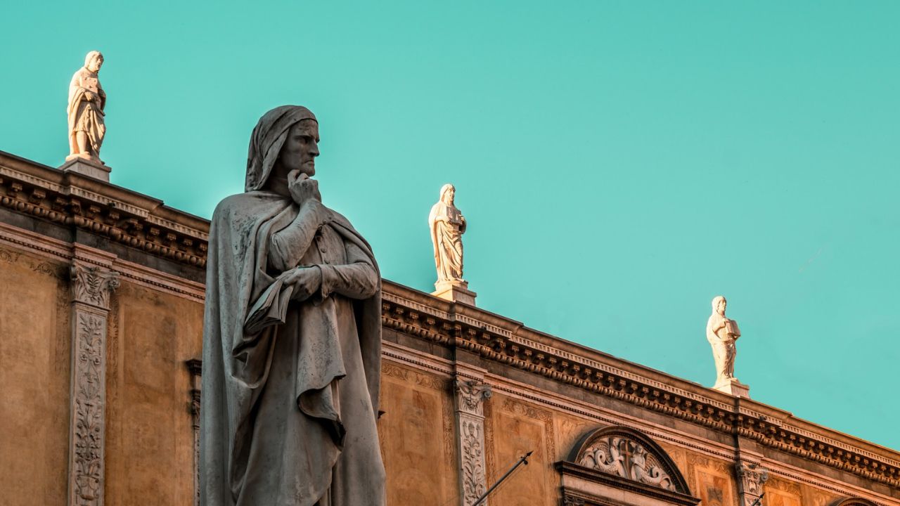 Socha muža na historickej budove pod modrou oblohou, s ďalšími sochami v pozadí.
