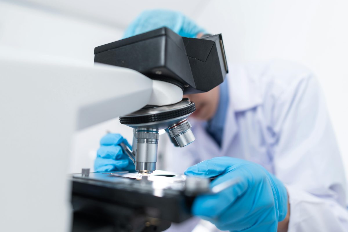Vedec v laboratórnom plášti používa mikroskop na výskum vzoriek v laboratóriu.