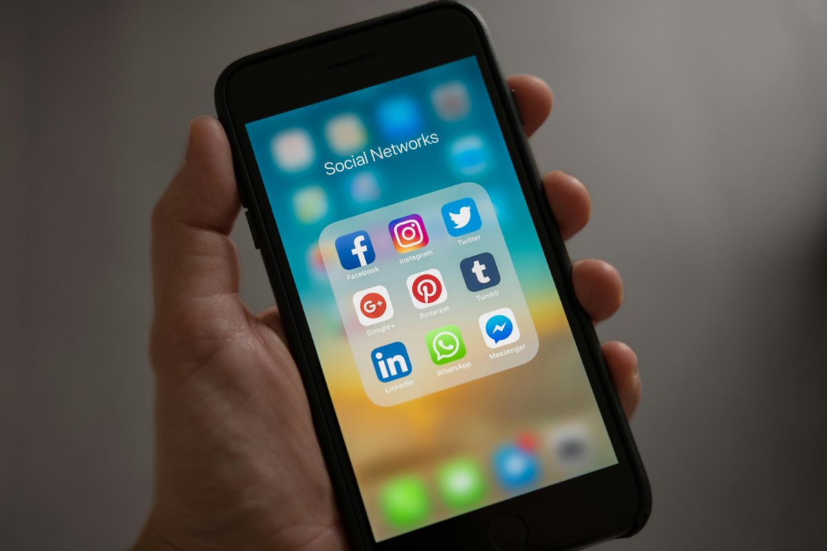 Ruka drží telefón so zobrazenými ikonami sociálnych sietí ako Facebook a Instagram na obrazovke.