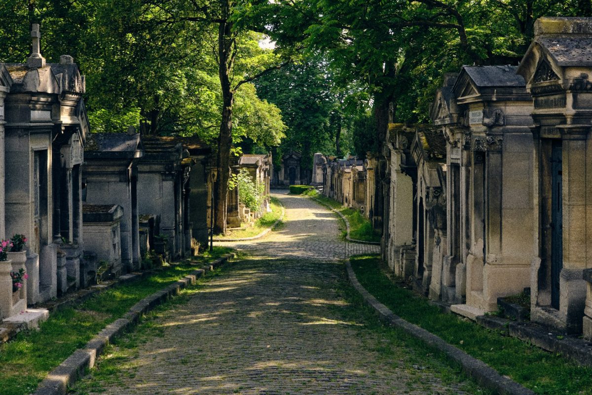 Hrobky pozdĺž dláždenej cesty v tieni stromov na starom cintoríne za slnečného dňa.