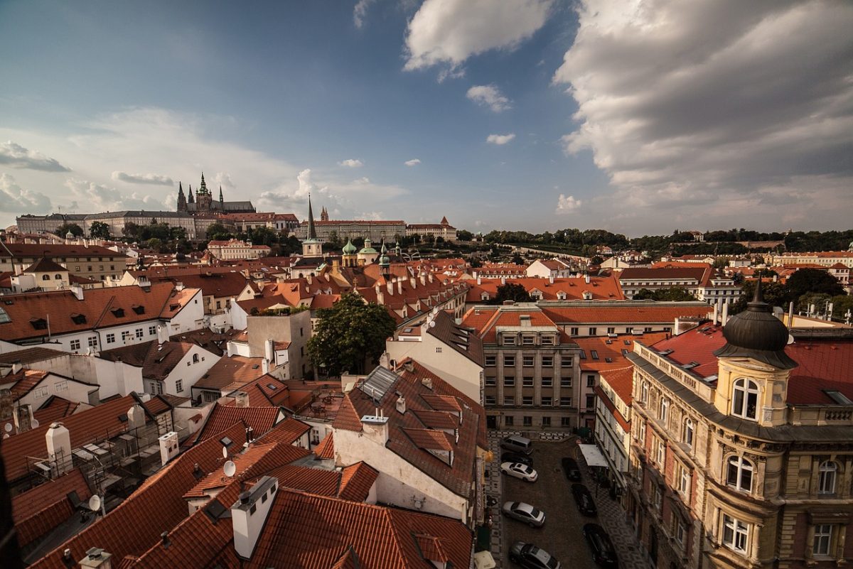 Panoráma historickej Prahy s pohľadom na červené strechy a oblohu, v pozadí vidieť Pražský hrad.