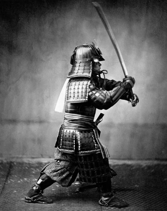 Samuraj v bojovej pozícii, drží meč pripravený na útok, historický japonský bojovník v tradičnom brnení.