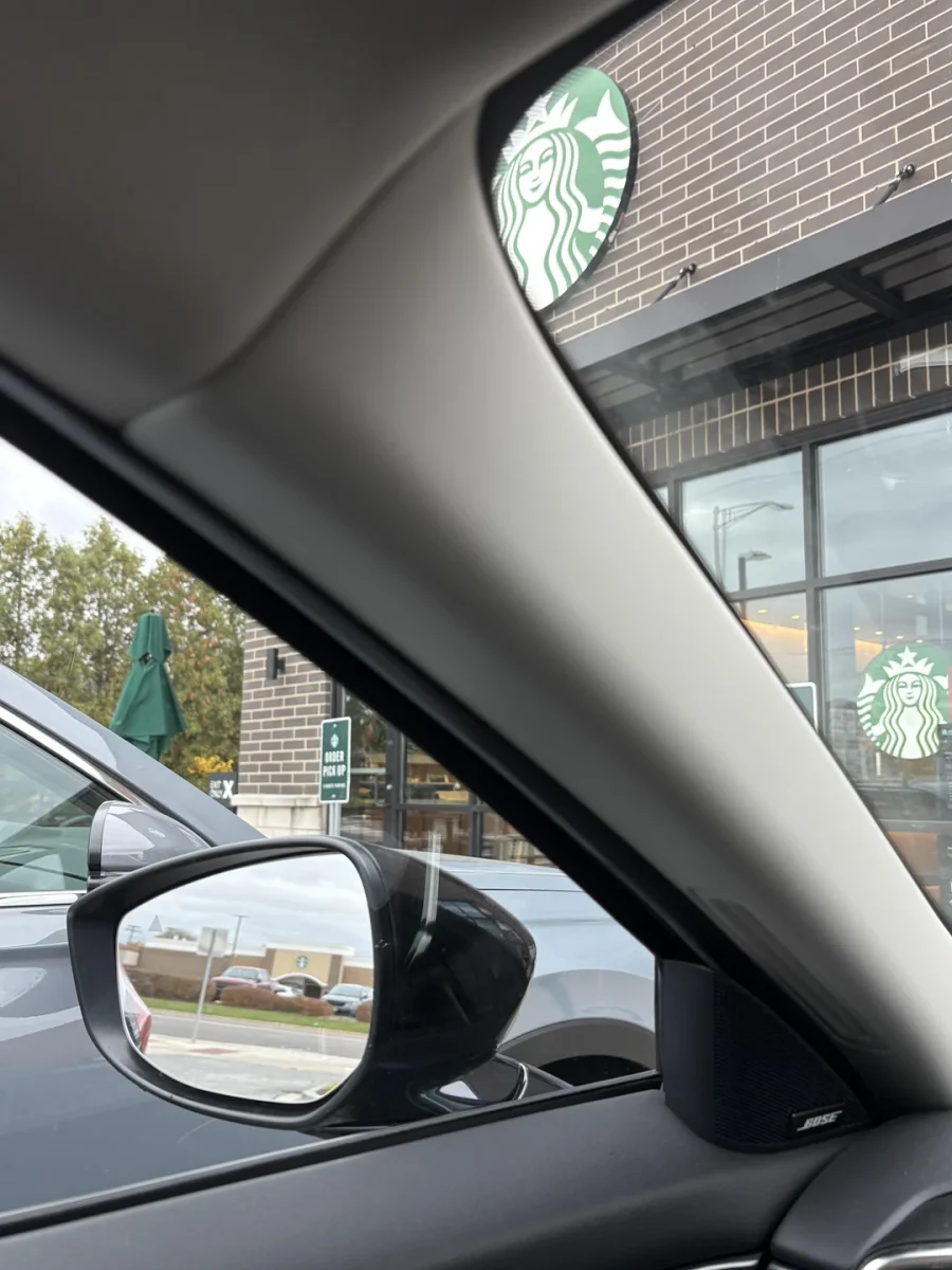 Auto zaparkované pred kaviarňou, logo na tehlovej fasáde je vidieť cez okno a spätné zrkadlo.