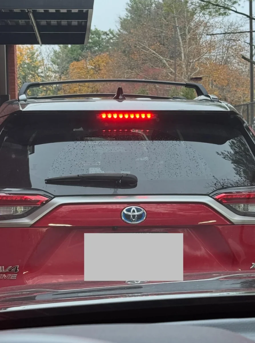 Červené SUV Toyota RAV4 s rozsvietenými brzdovými svetlami stojí v rade pri jeseňou sfarbených stromoch.