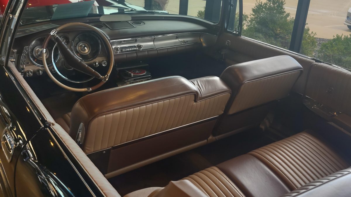 Interiér veteránu s koženými sedadlami a dreveným volantom v retro štýle z pohľadu zadného sedadla.