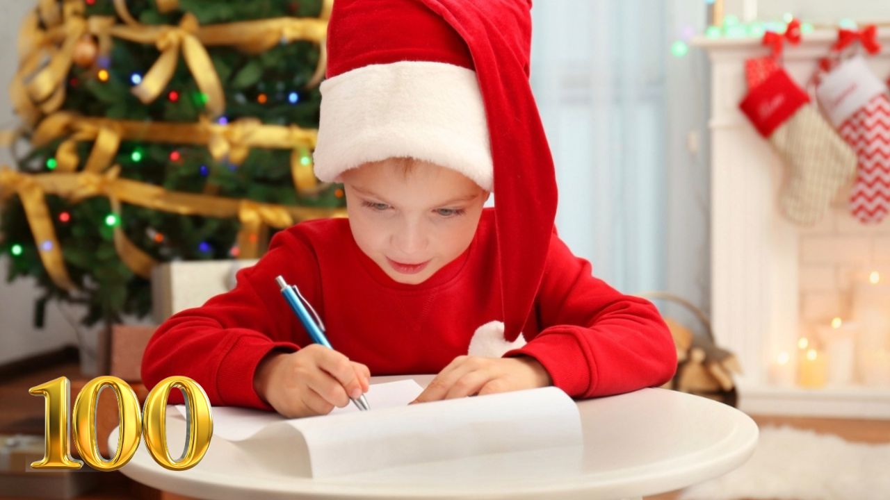 Chlapec v mikine so santovskou čiapkou píše list na Vianoce pri ozdobenom stromčeku.