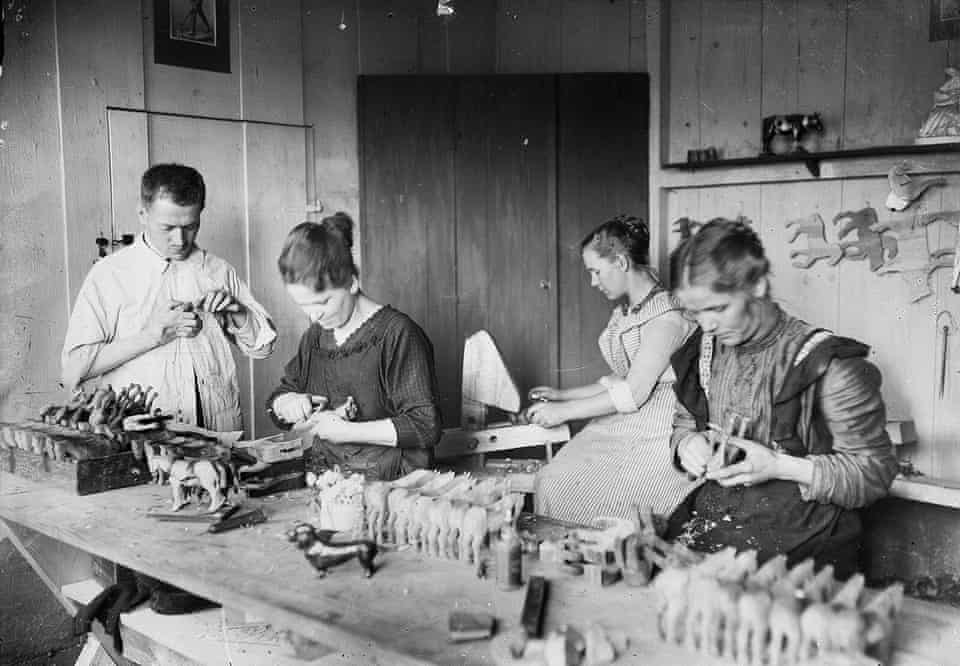 Historická dielňa: štyria remeselníci ručne vyrábajú drevené hračky pri drevenom stole.