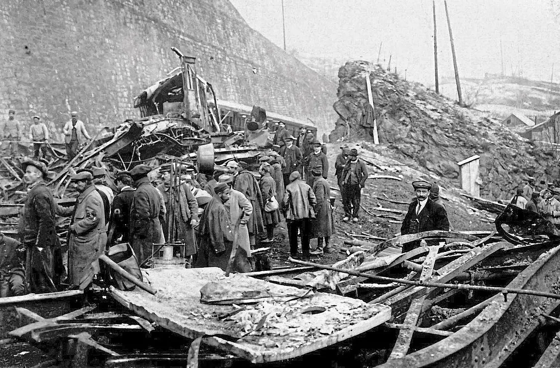 Skupina ľudí skúma trosky vlaku po nehode v hornatej oblasti za hmlistého počasia.