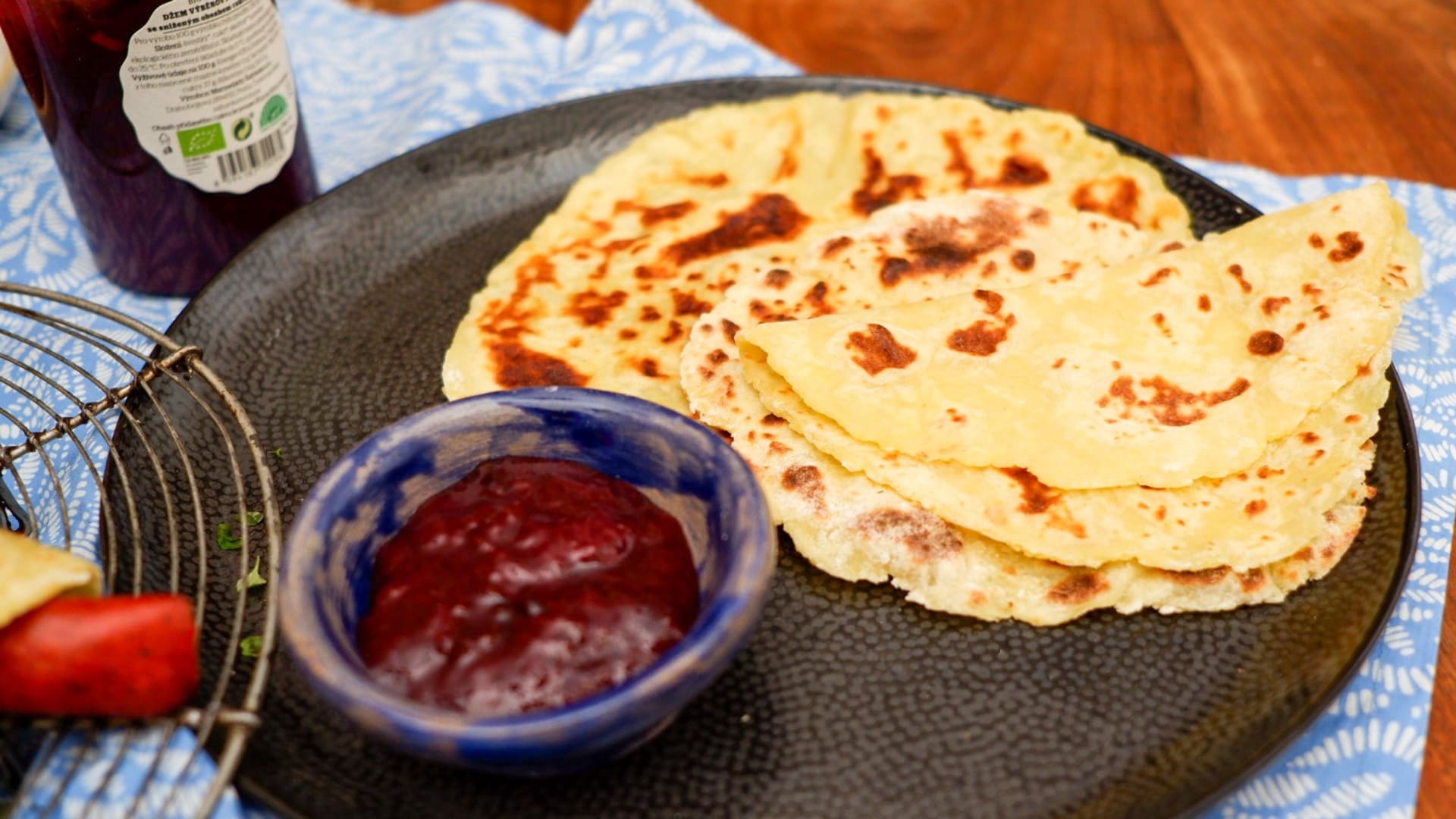 Domáce palacinky na tmavom tanieri s miskou jahodového džemu.