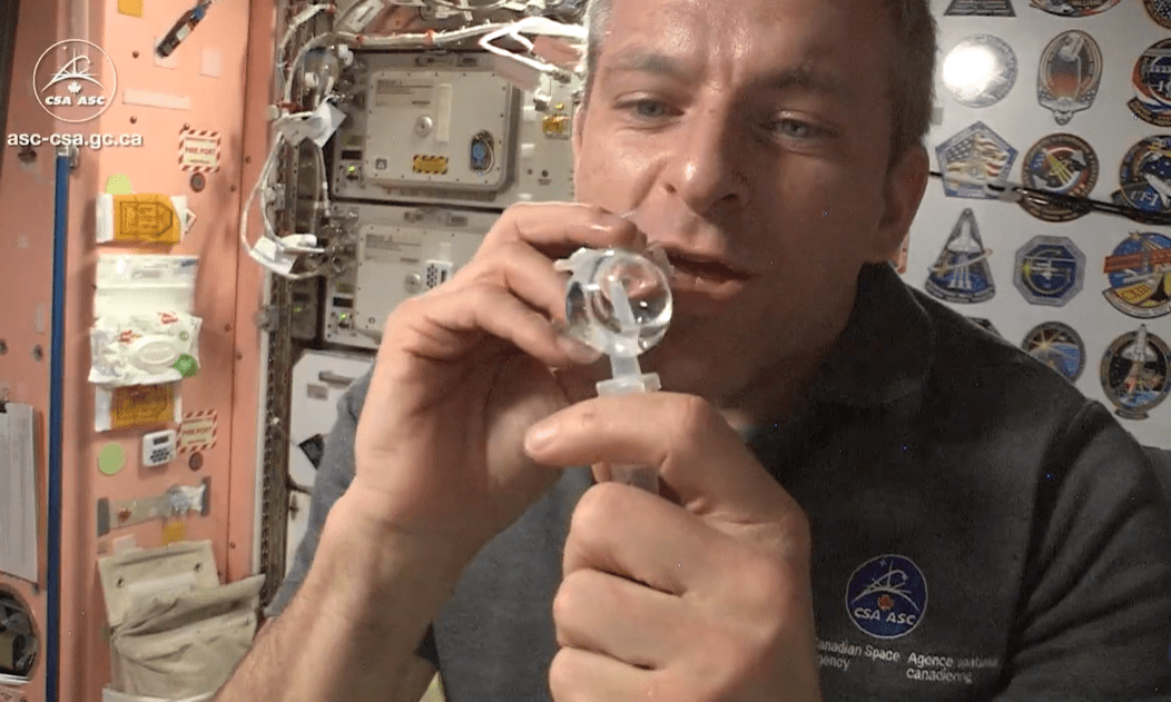 Astronaut skúma vodnú kvapku vo vesmíre na vesmírnej stanici plnej technologických prístrojov.