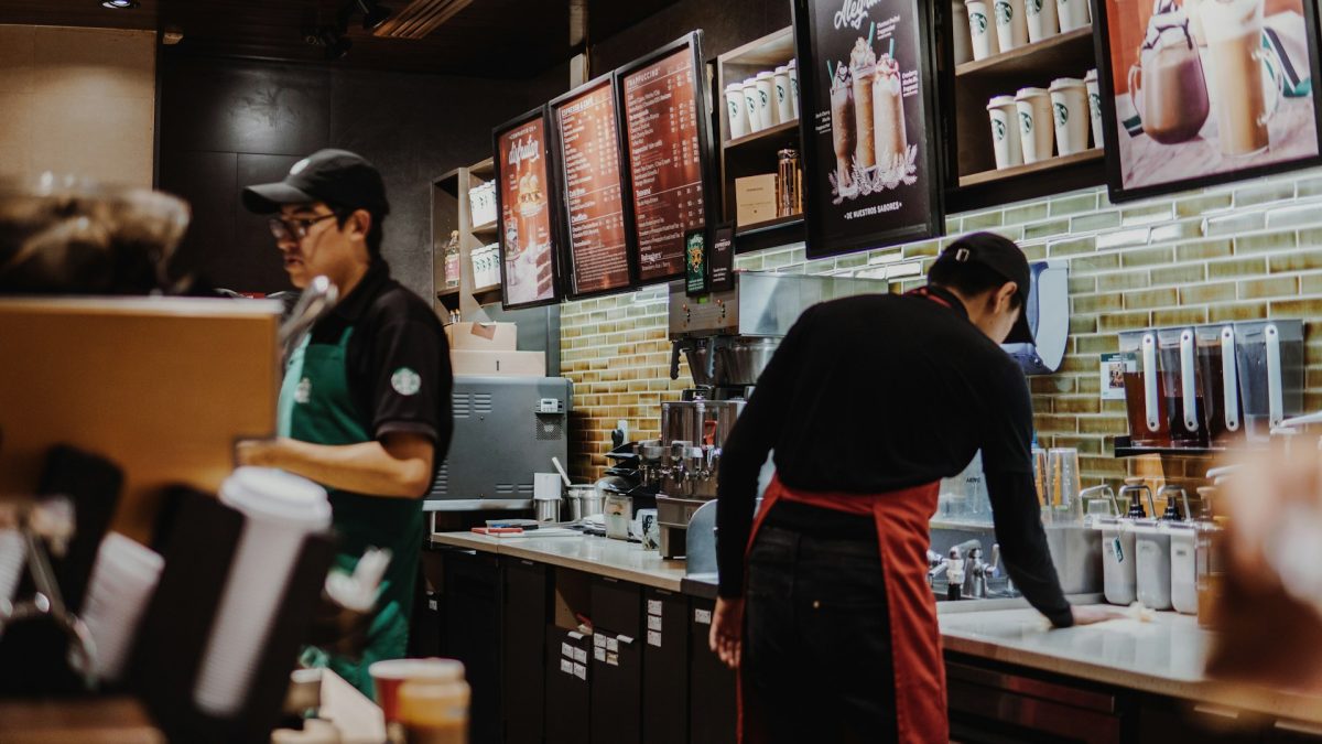 Baristi pripravujú kávu v modernej kaviarni s menu na stene a praktických pomôckach na každom kroku.