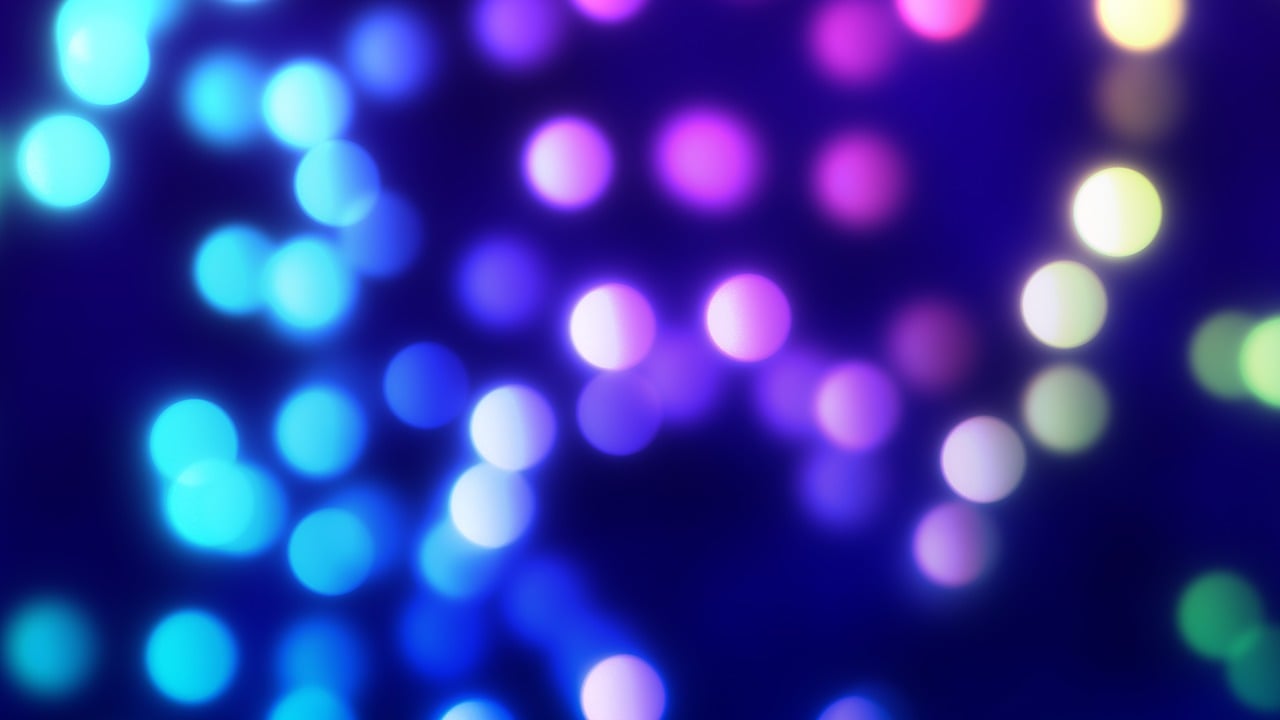 Farebný bokeh efekt s modrými a fialovými svetlami na tmavom pozadí, vytvárajúci snovú atmosféru.