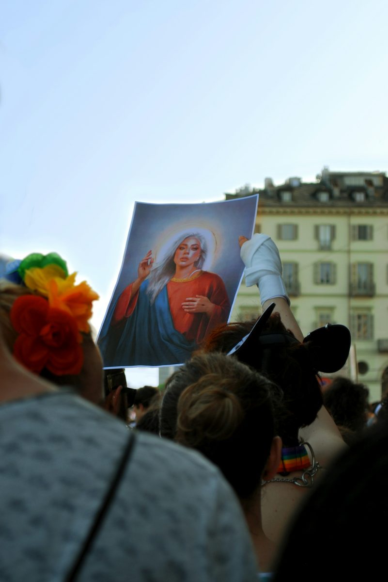 Skupina ľudí držiacich obraz so svätožiarou na verejnom podujatí, budovy v pozadí.
