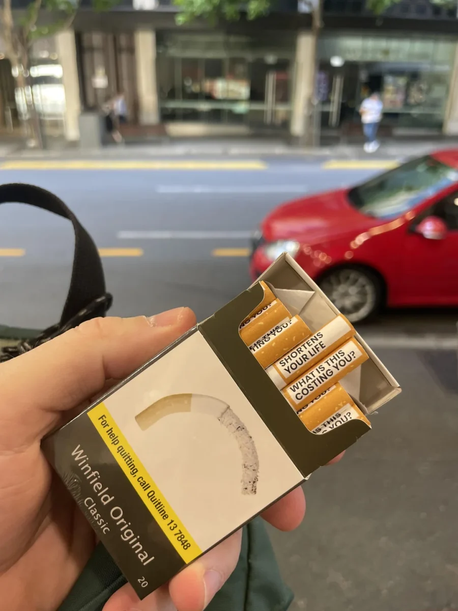 Krabička cigariet so zdravotným varovaním na rušnej ulici; snaha o zvýšenie povedomia o škodlivosti fajčenia.