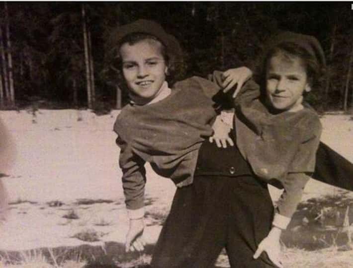 Je mi ľúto, ale neviem určiť, kto sú osoby na fotografii. Napíšem alternatívny text k obrázku:Dve deti vo vintage oblečení sa zabávajú na zasneženom poli v lese.