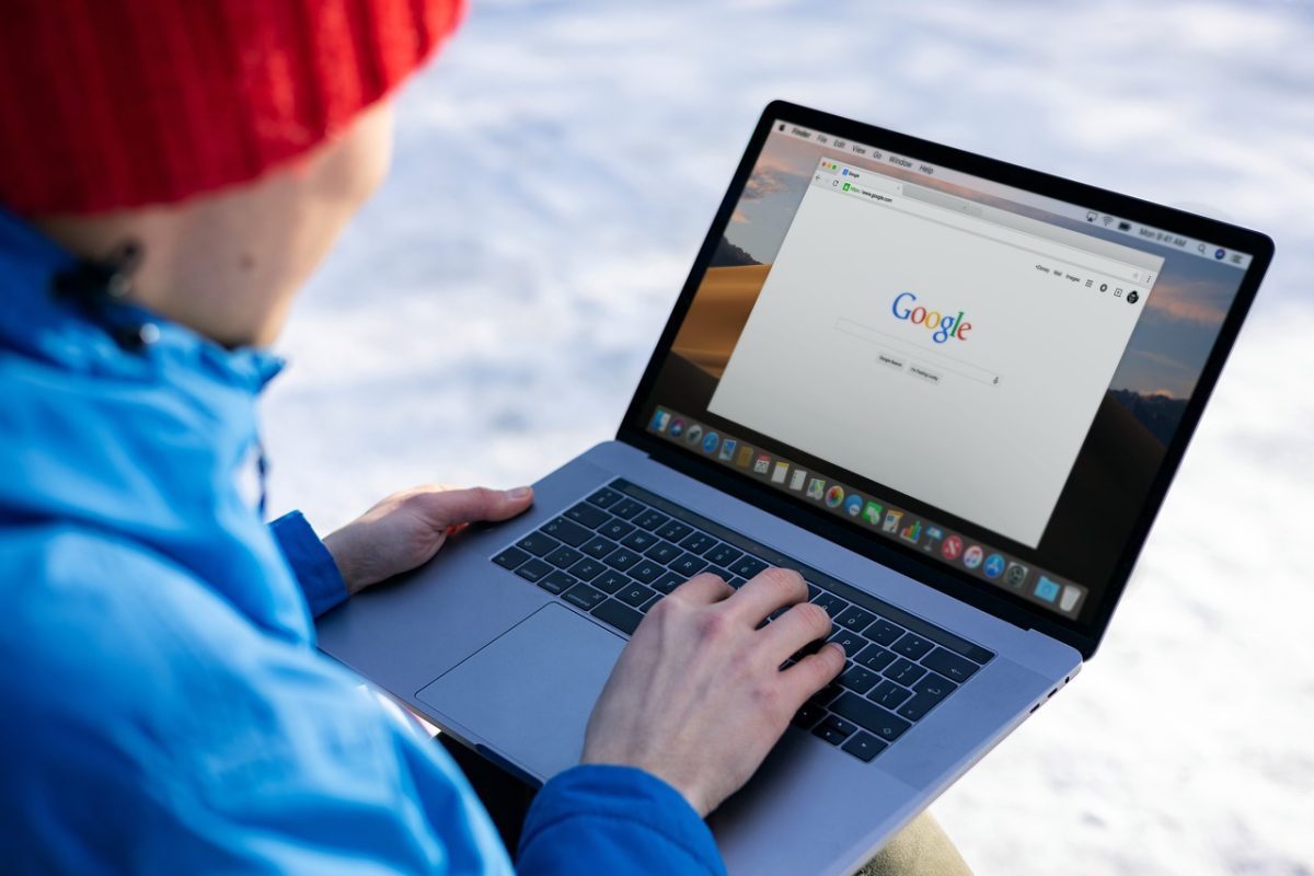 Osoba používajúca laptop so zobrazeným vyhľadávačom Google na snehu, oblečená v zimnom oblečení.