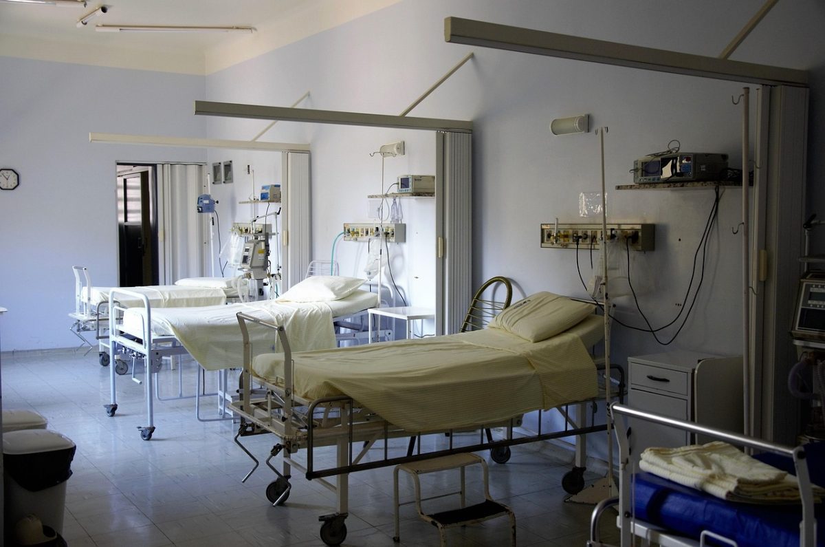 Prázdna nemocničná izba s troma lôžkami, medicínskym zariadením a bielymi stenami.