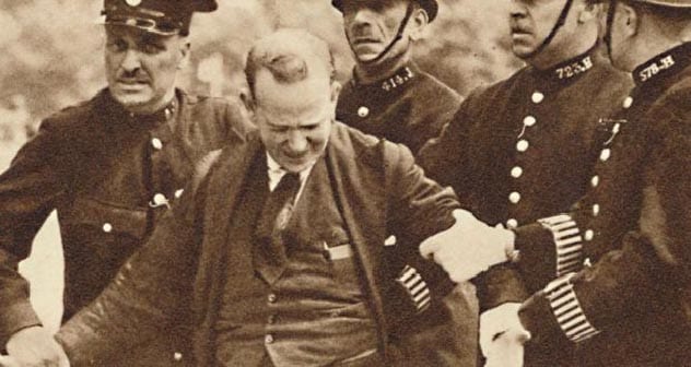 Policajti zatýkajú muža počas protestu, historická fotografia zachytáva súdny incident z minulosti.