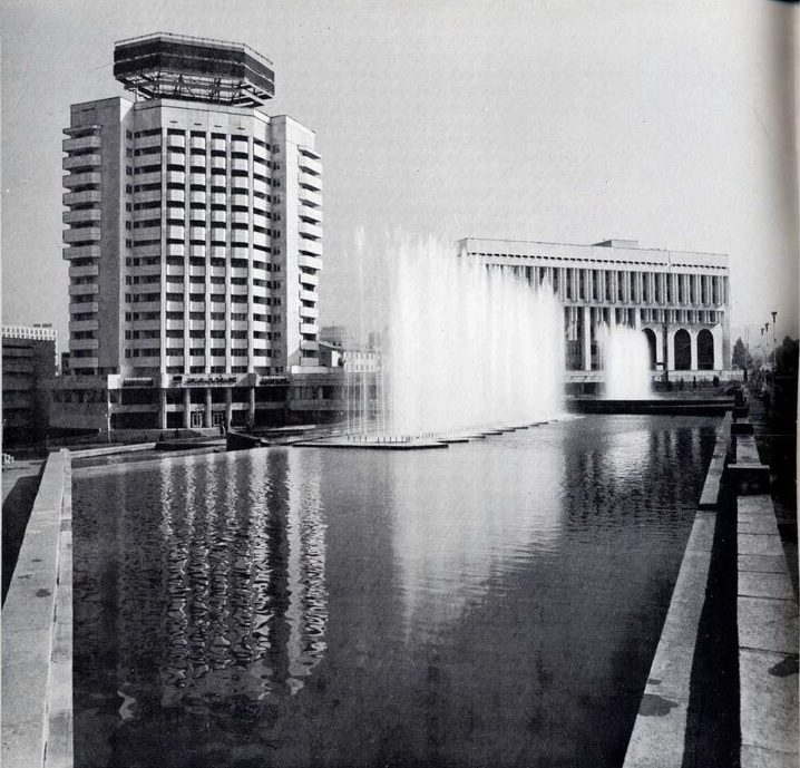 Moderné budovy s fontánou v popredí, čiernobiela fotografia.