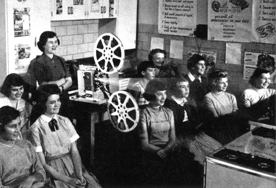 Skupina študentov sleduje film v triede so starým filmovým projektorom. Atmosféra 50. rokov minulého storočia.