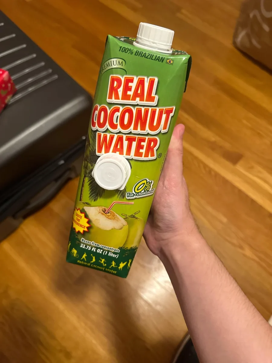 Krabička nápoja z kokosovej vody značky Real Coconut Water v ruke na drevenej podlahe.