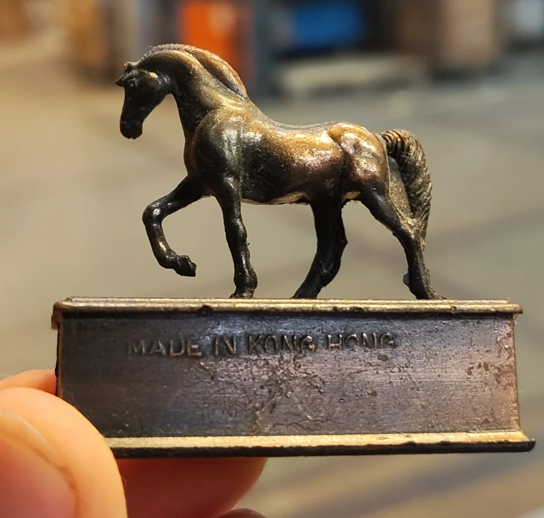 Malá kovová soška koňa na podstavci s nápisom Made in Hong Kong.