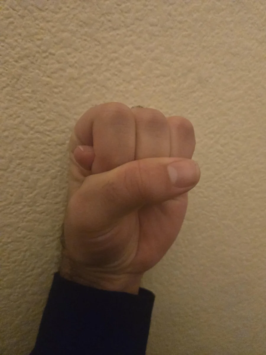 Ruka zatvorená v päsť, položená na jemne textúrovanú stenu, zobrazuje gesto sily a odhodlania.
