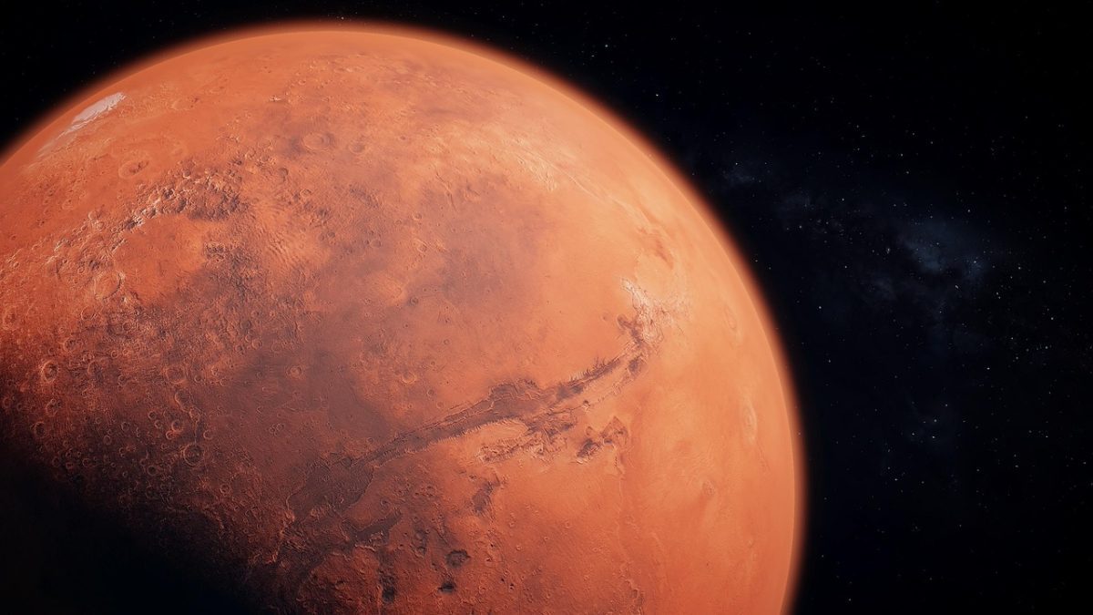 Planéta Mars vo vesmíre, zobrazená zblízka s viditeľnými krátermi a kaňonmi na oranžovom povrchu.