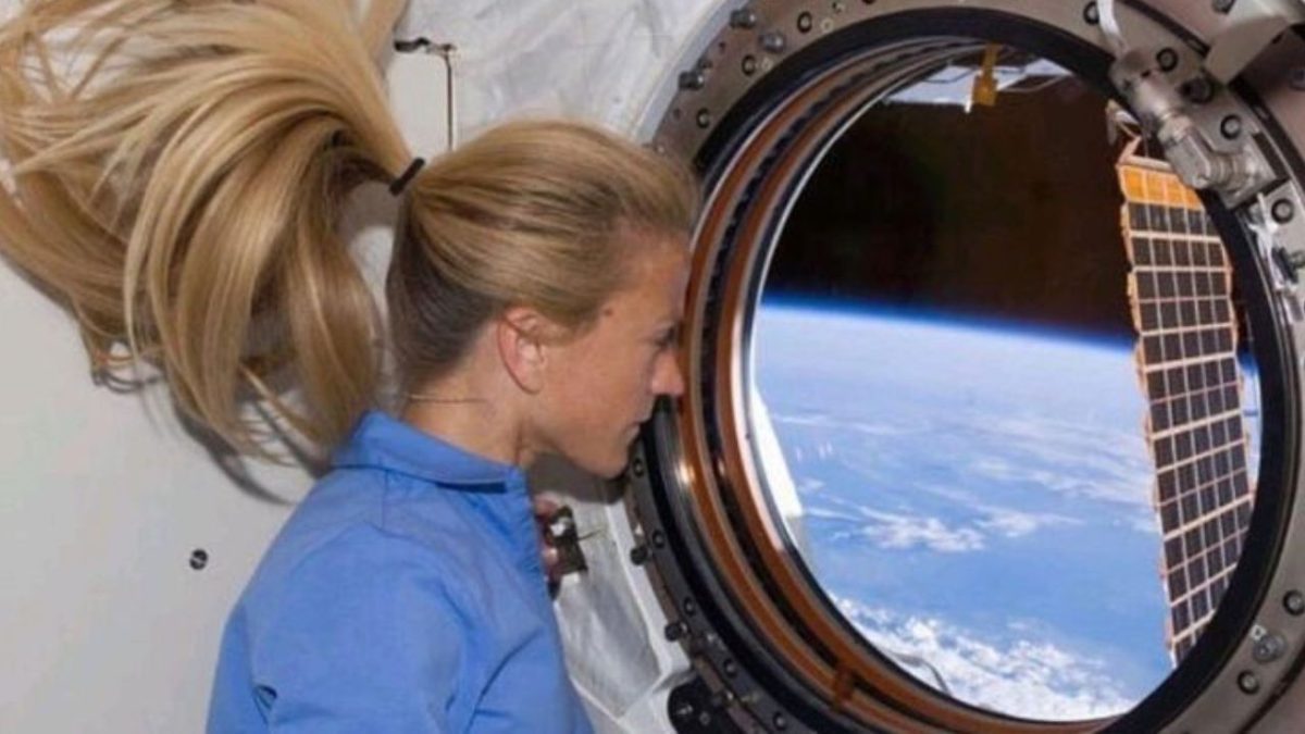 Astronautka sleduje Zem cez okno vesmírnej stanice, vlasy jej voľne plávajú v beztiažovom stave.