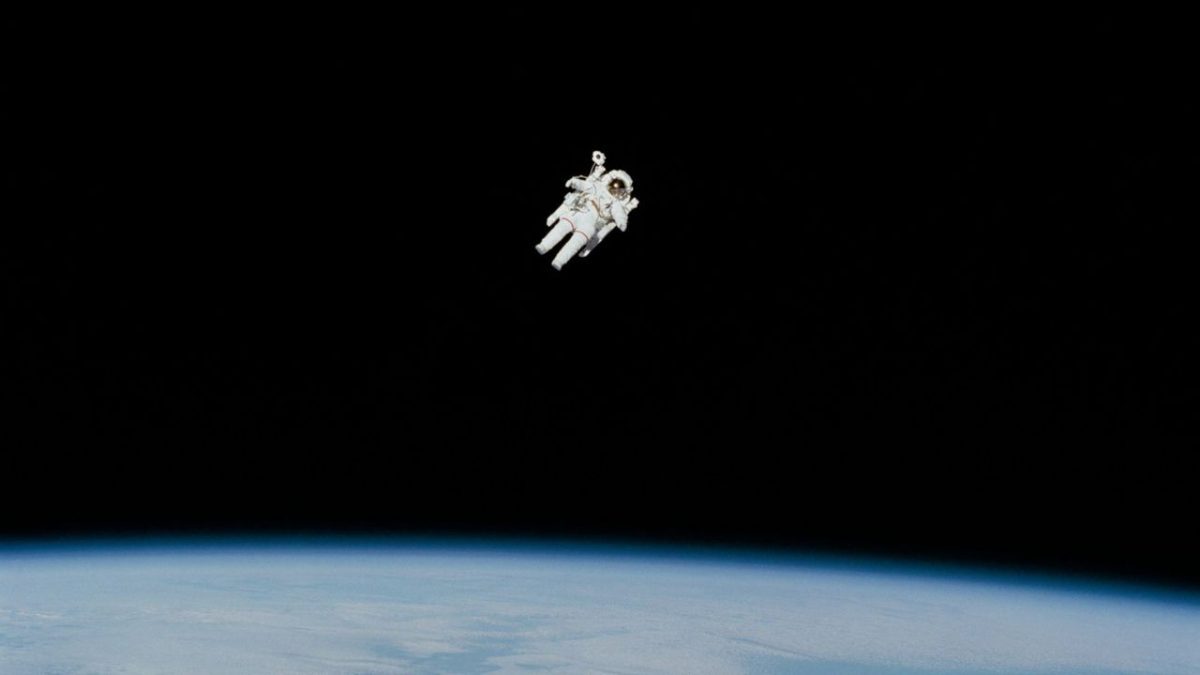 Astronaut vo vesmíre plávajúci nad Zemou v otvorenom vesmíre.