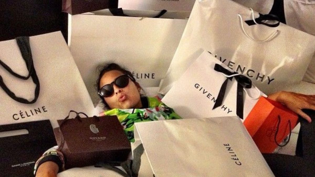 Žena v okuliaroch obklopená luxusnými nákupnými taškami od značiek Céline a Givenchy.