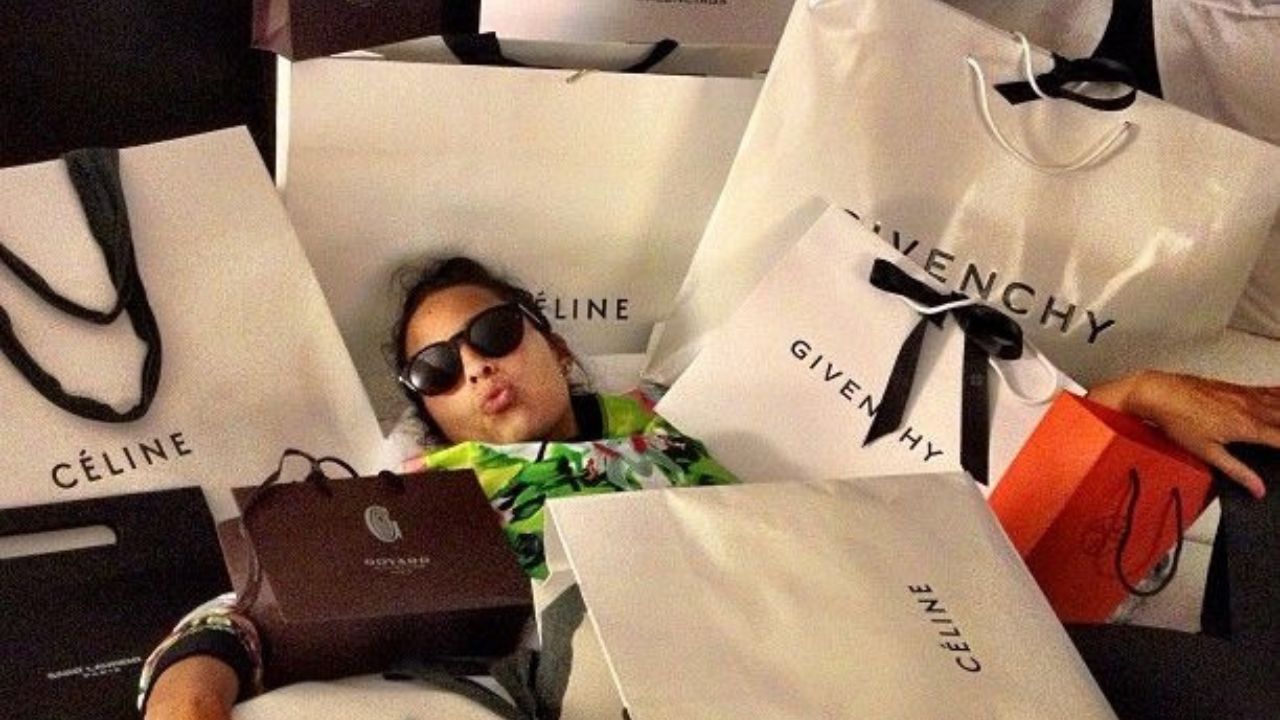 Žena v okuliaroch obklopená luxusnými nákupnými taškami od značiek Céline a Givenchy.