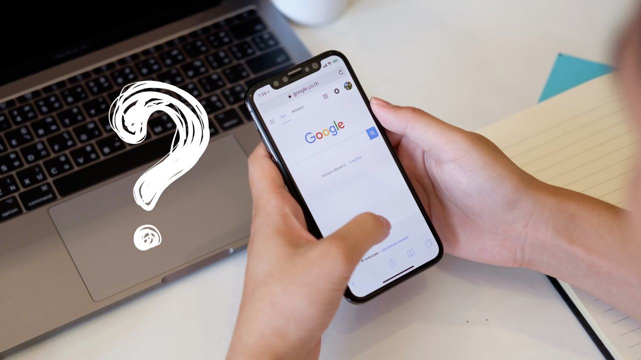 Osoba hľadá niečo na Google v smartfóne pred otvoreným notebookom a otáznikom.