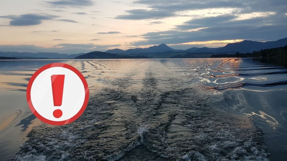 Obrázok západu slnka nad pokojným jazerom s výrazným varovným symbolom v popredí.