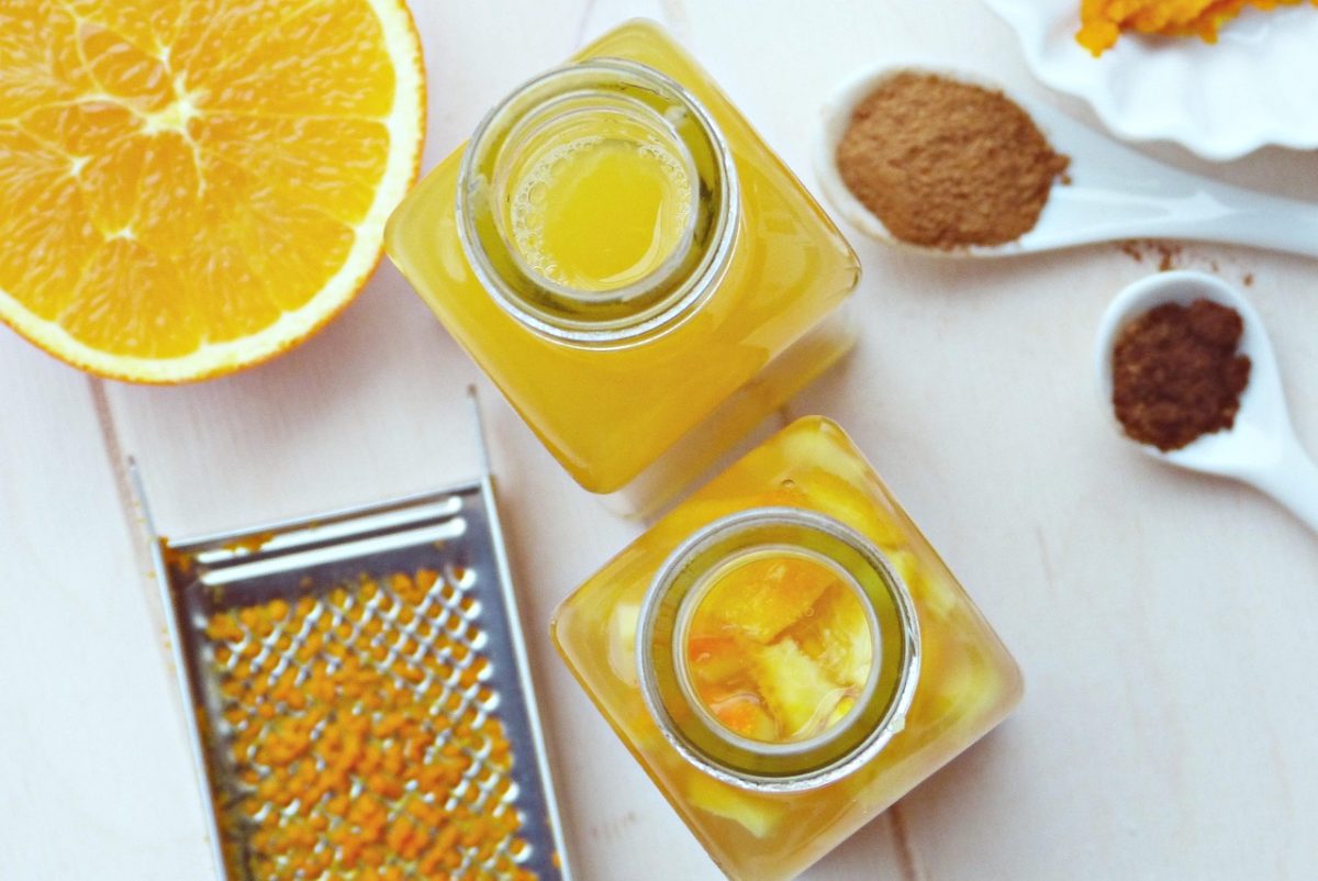 Čerstvá pomarančová šťava a koreniny na bielom stole, zblízka pohľad na ingrediencie pre zdravý nápoj.