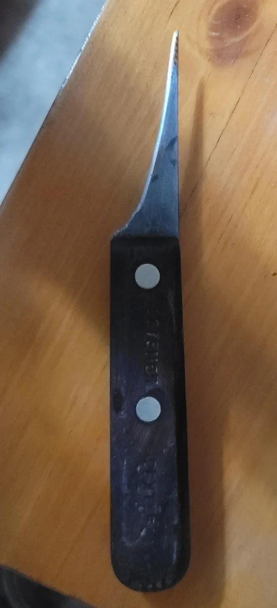 Malý nôž s čiernou rukoväťou a oceľovou čepeľou na drevenom stole.