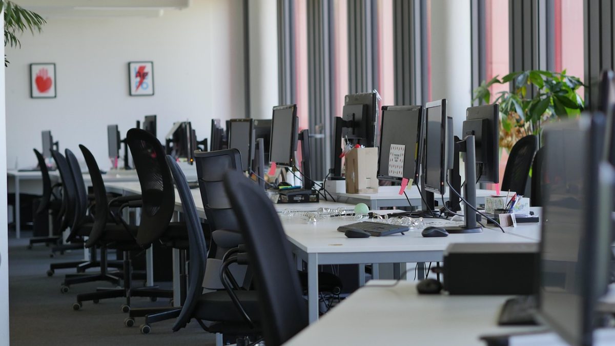 Prázdna kancelária s modernými počítačmi a ergonomickými stoličkami, pripravená na pracovný deň.