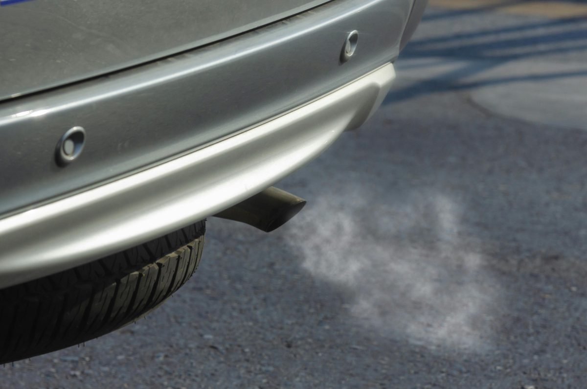 Auto s výfukom vypúšťajúcim dym na asfaltovej ceste. Ekologická problematika výfukových plynov.