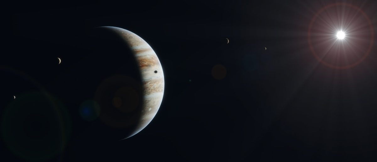 Planéta Jupiter so štyrmi jeho mesiacmi osvetlená slnkom na tmavej nočnej oblohe.