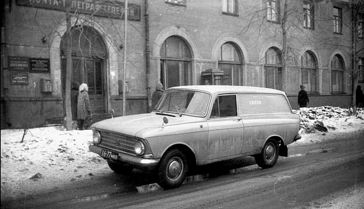 Historický automobil parkuje na zasneženej ulici pred budovou, kde kráčajú ľudia v zimnom oblečení.