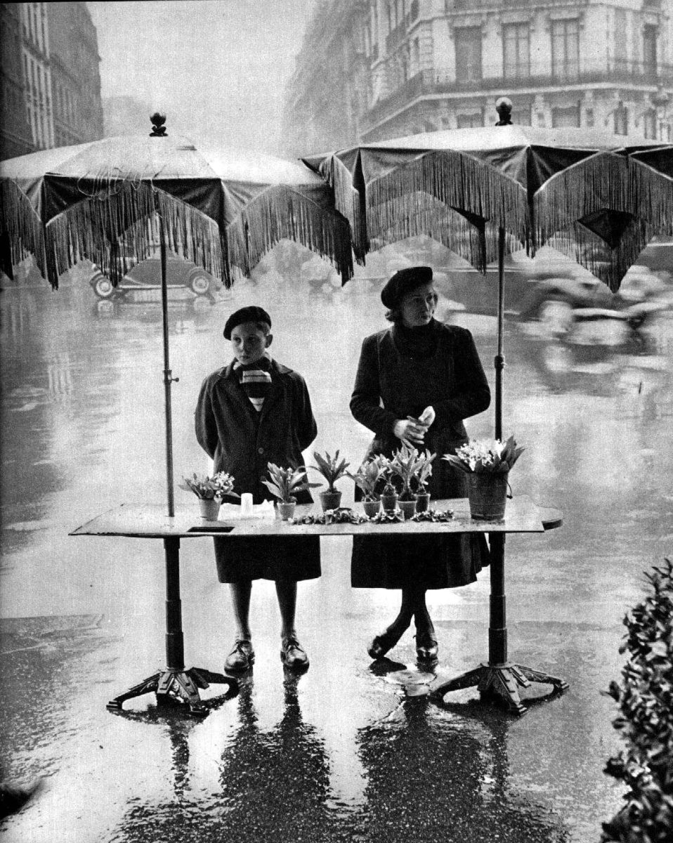 Dve osoby pod dáždnikmi na dažďovej ulici ponúkajú kvety na predaj. Retro atmosféra.