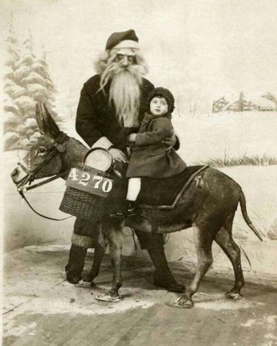 Muž so Santa klobúkom a dievča na oslíkovi v zasneženej krajine, historická vianočná fotografia.